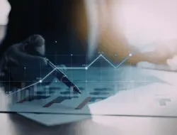 Mão segurando uma caneta sobre documentos financeiros, com gráfico de linhas e barras sobreposto indicando crescimento e evolução de indicadores ao longo do tempo.