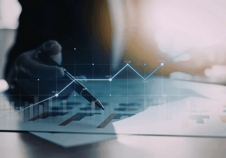 Mão segurando uma caneta sobre documentos financeiros, com gráfico de linhas e barras sobreposto indicando crescimento e evolução de indicadores ao longo do tempo.
